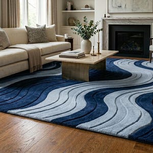 Op de afbeelding: Een rechthoekig vloerkleed met een herhalend patroon van golvende, vloeiende lijnen in verschillende tinten diep marineblauw en licht hemelsblauw. Het kleed heeft een getextureerd, uitgesneden uiterlijk met verhoogde delen voor diepte en beweging.
