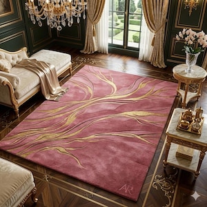 Könnte beinhalten: Ein rechteckiger, rosafarbener Teppich mit einem goldenen, abstrakten Design. Der Teppich hat eine weiche, plüschige Textur und befindet sich in einem luxuriösen Raum. Die Initialen "AR" sind dezent in der unteren rechten Ecke gestickt. Der Teppich misst ca. 244 x 305 cm.
