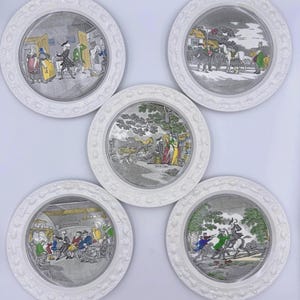May include: Set of five white decorative plates with detailed, grayscale illustrations depicting historical scenes. Each plate has a textured, raised border. The illustrations feature figures in period clothing, with accents of color.