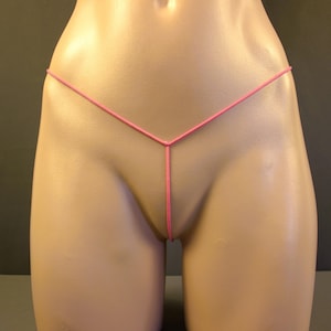 May include: A close-up view of a mannequin torso wearing a pink thong. The thong is made of a thin, string-like material and features a simple design. The background is a neutral color.