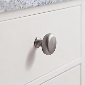 Può includere: Primo piano di un cassetto di un mobile bianco con una manopola in nichel spazzolato. Il cassetto fa parte di un mobile bianco con un piano di lavoro maculato grigio. La manopola è di forma ovale e proietta un'ombra sul cassetto.