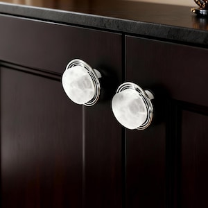 Könnte beinhalten: Nahaufnahme eines dunkelbraunen Schranks mit zwei weißen und silbernen Schrankknöpfen. Die Knöpfe sind rund mit marmoriertem Aussehen und von einem silbernen Ring umgeben. Der Schrank hat eine dunkle Arbeitsplatte.