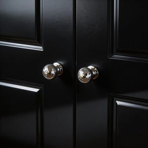 Op de afbeelding: Close-up van twee zwarte kastdeuren met zilveren en chromen bolvormige knoppen. De knoppen hebben een facetontwerp dat licht reflecteert. De deuren hebben een glanzende afwerking en verzonken panelen.