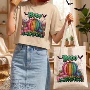 Puede incluir: Una camiseta corta de color beige y una bolsa de tela a juego, ambas con un gráfico de una calabaza colorida con el texto BOOO y Sweet or Trick, rodeada de murciélagos, telarañas y pequeños fantasmas en tonos verdes y morados.
