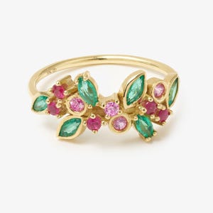 May include: A gold ring featuring a cluster of marquise-cut green stones and round-cut pink and red stones arranged in a leaf-like pattern. The band is thin and polished gold, with the stones set in a decorative, asymmetrical arrangement across the top.