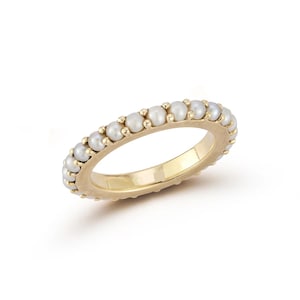 May include: A gold ring featuring a continuous row of small, white pearls. The ring has a smooth, polished gold band and the pearls are evenly spaced around the circumference. The ring is a classic piece of jewelry.