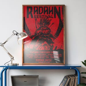 May include: A blue metal table with a framed red poster that reads "RADAHN FESTIVAL" and a black graphic. A silver record player sits on the table, along with a stack of vinyl records. A silver desk lamp is on the table.
