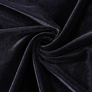 May include: A deep black velvet fabric featuring a dense, soft pile texture. The material is gathered in the center, creating natural folds and highlights that emphasize the light-reflecting quality of the dark, plush surface of the textile.
