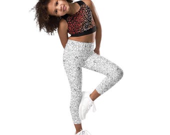 May include: A young person wearing a black and red leopard print sports bra and white leggings with a black and white cartoon character pattern. The person is also wearing white sneakers.
