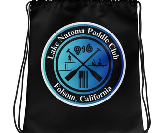 May include: Black drawstring bag featuring a circular logo for the Lake Natoma Paddle Club. The logo includes the text "Lake Natoma Paddle Club", "916", and "Folsom, California". The logo also features paddle sports imagery and an American flag.