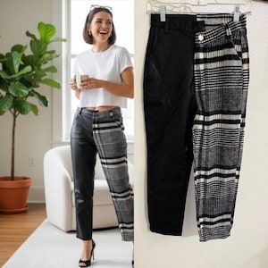 May include: Black and gray plaid and black faux leather pants. The pants are split down the middle, with one side featuring a black faux leather material and the other side a black and gray plaid pattern. The pants are hanging on a hanger.