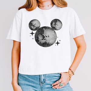 A woman wearing a white t-shirt with a graphic design of three disco balls and stars on it.