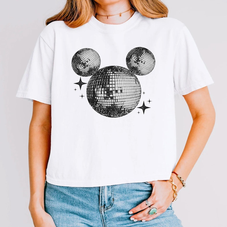A woman wearing a white t-shirt with a graphic design of three disco balls and stars on it.