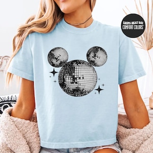 A woman wearing a light blue t-shirt with a graphic of a disco ball and stars printed on it.