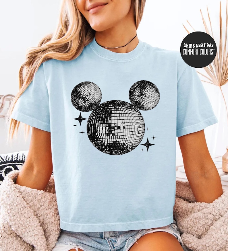 A woman wearing a light blue t-shirt with a graphic of a disco ball and stars printed on it.