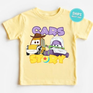A yellow t-shirt with a cartoon image of two cars, one with a cowboy hat and the other with a green and purple design, along with the text "CARS STORY".