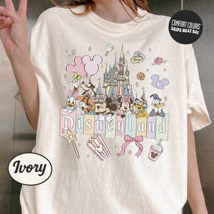 A person is wearing a white t-shirt with a Disney-themed graphic design featuring Mickey Mouse, Minnie Mouse, Donald Duck, and other Disney characters.