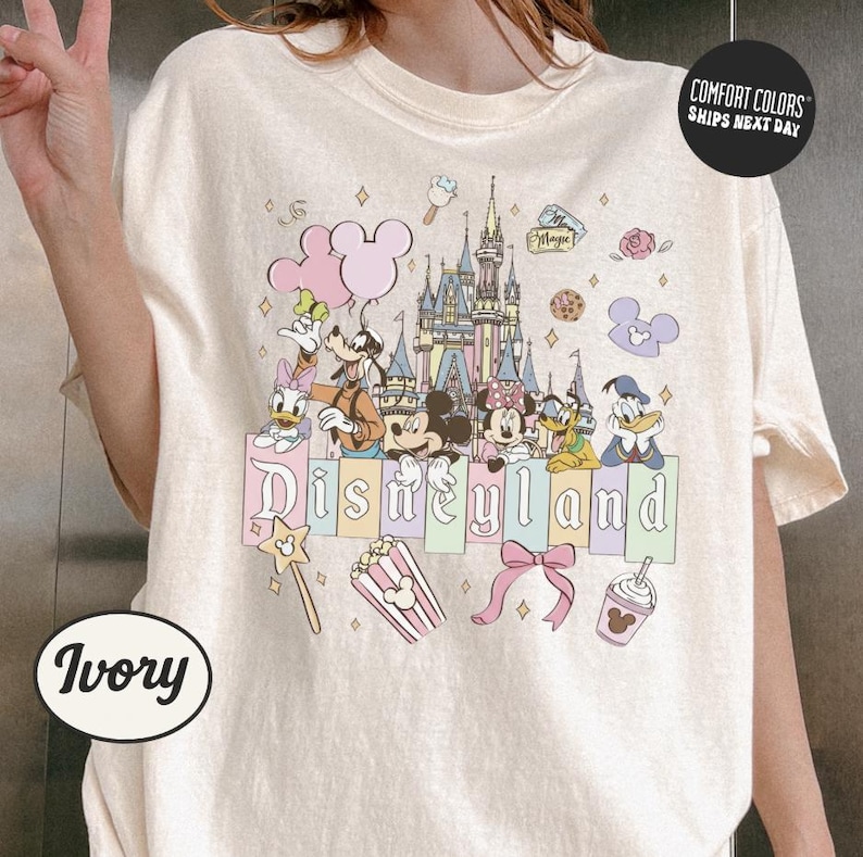 A person is wearing a white t-shirt with a Disney-themed graphic design featuring Mickey Mouse, Minnie Mouse, Donald Duck, and other Disney characters.