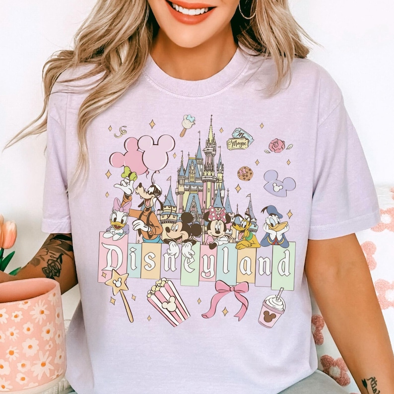 A woman wearing a t-shirt with a Disney-themed graphic design, including Mickey Mouse, Minnie Mouse, Donald Duck, and other iconic Disney characters.