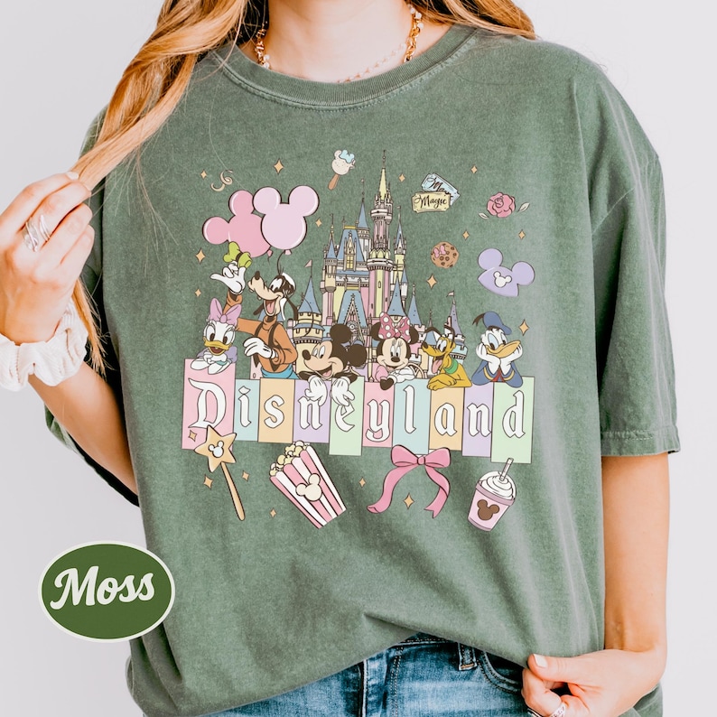 A woman wearing a green t-shirt with a Disney-themed graphic of Mickey Mouse, Minnie Mouse, Donald Duck, and other Disney characters.