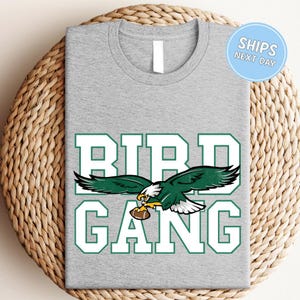 A gray t-shirt with a graphic design featuring a green eagle holding a football, along with the text "BIRD GANG" printed on it.