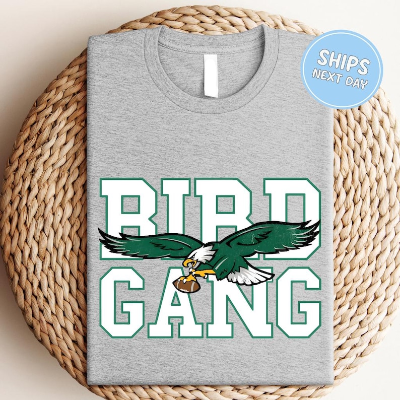A gray t-shirt with a graphic design featuring a green eagle holding a football, along with the text "BIRD GANG" printed on it.
