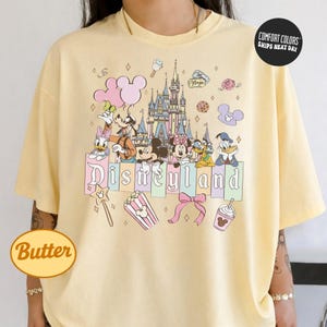 A person wearing a yellow t-shirt with a Disney-themed graphic design featuring Mickey Mouse, Minnie Mouse, Donald Duck, and other Disney characters.