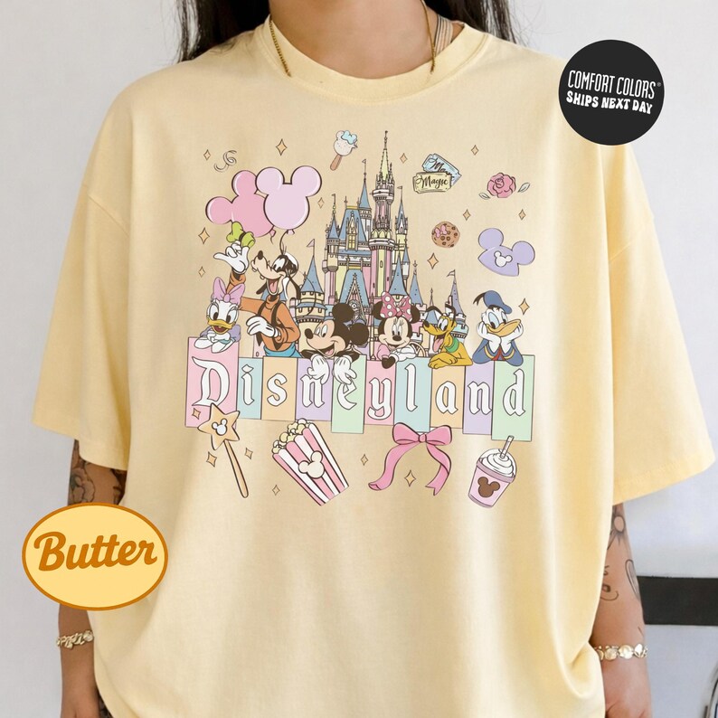 A person wearing a yellow t-shirt with a Disney-themed graphic design featuring Mickey Mouse, Minnie Mouse, Donald Duck, and other Disney characters.