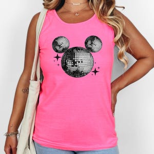 A woman wearing a pink tank top with a graphic of a disco ball and stars on it.
