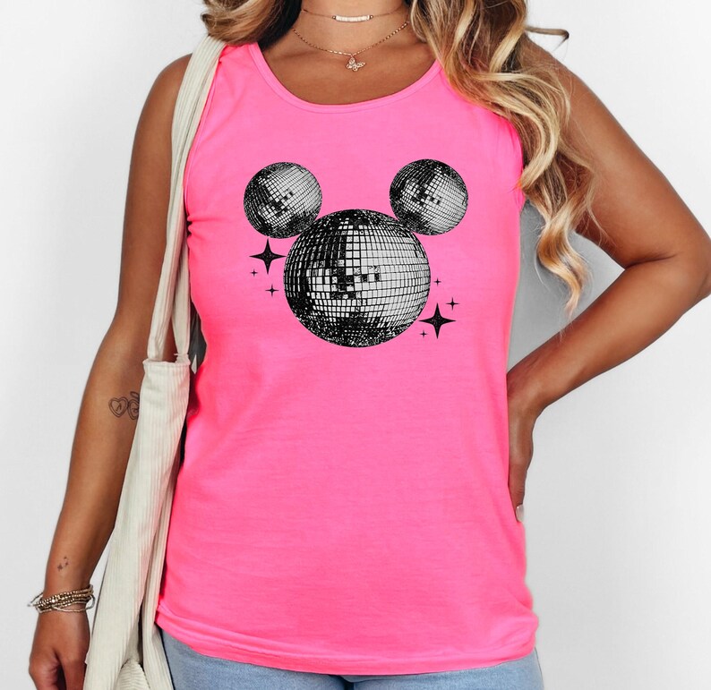 A woman wearing a pink tank top with a graphic of a disco ball and stars on it.