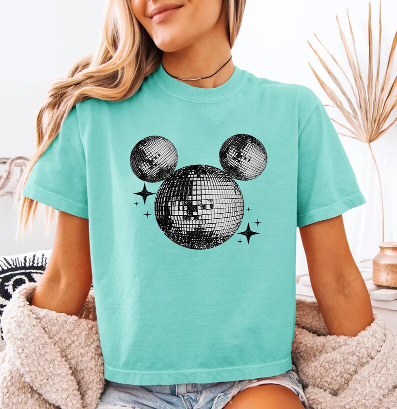 A woman wearing a turquoise t-shirt with a graphic of a disco ball and stars on it.