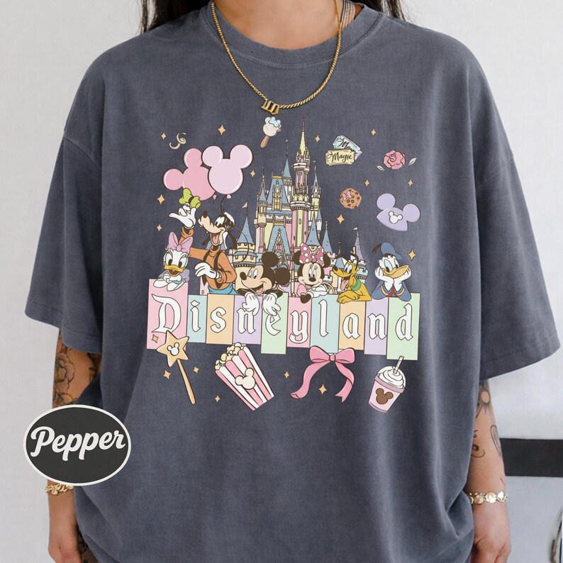 A person wearing a gray t-shirt with a Disney-themed graphic design featuring Mickey Mouse, Minnie Mouse, Donald Duck, and other Disney characters, along with the word "Disneyland" prominently displayed.