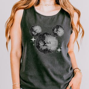 A woman wearing a gray tank top with a graphic of two disco balls and stars on it.