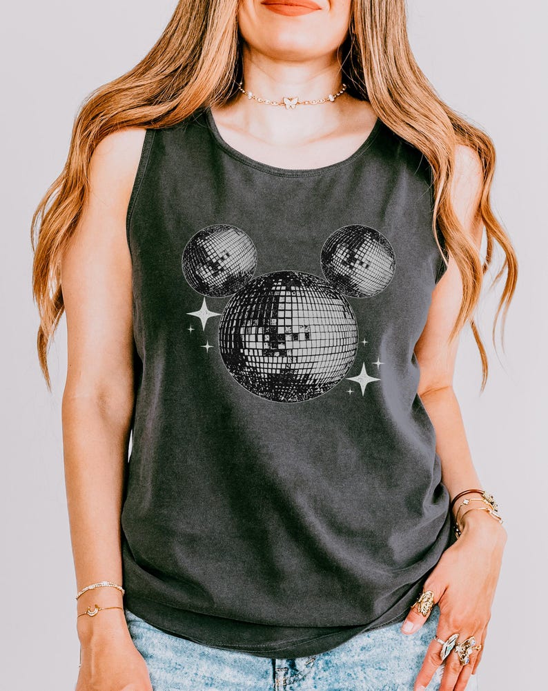 A woman wearing a gray tank top with a graphic of two disco balls and stars on it.