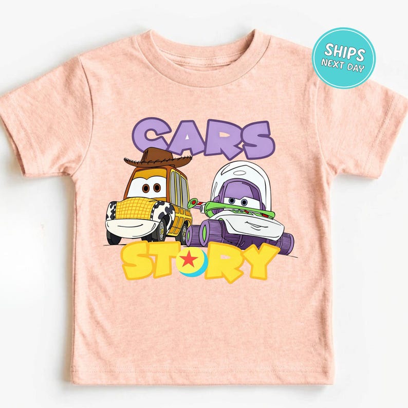 A pink t-shirt with a graphic design featuring two cartoon cars, one yellow and one purple, along with the text "CARS STORY" and a character from the Toy Story movie.