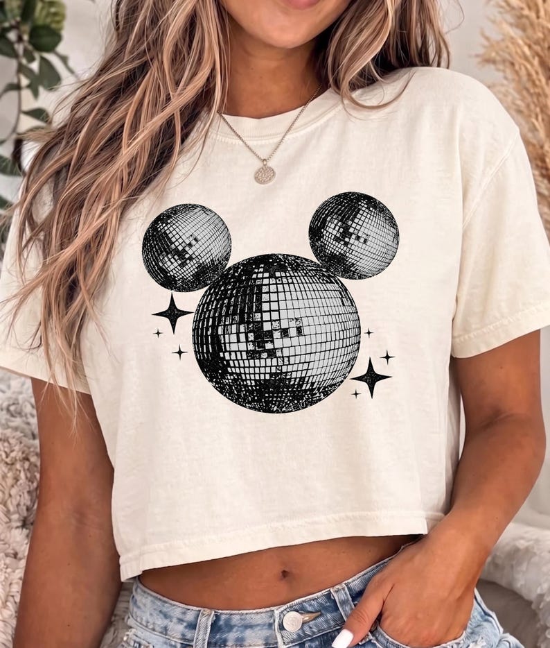 A woman wearing a white crop top with a graphic of two disco balls and stars on it.