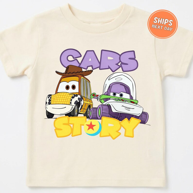 A white t-shirt with a graphic design featuring two cartoon cars, one yellow and one purple, along with the text "CARS STORY" and a character wearing a cowboy hat.