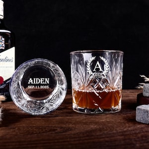 May include: Two engraved whiskey glasses with a diamond-cut pattern. One glass contains amber liquid. The glasses are inscribed with the name "AIDEN" and the date "SEP.11.2025". One glass features the letter "A" within a laurel wreath.