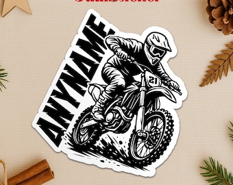 May include: Black and white sticker featuring a motocross rider on a dirt bike. The sticker has the text "ANYNAME" in a bold, slanted font. The rider is wearing a helmet and goggles. The sticker is a graphic design.