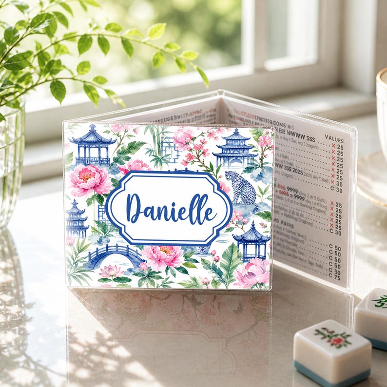 May include: A personalized, clear acrylic menu holder featuring a floral and pagoda design with the name "Danielle" in a blue frame. The design includes pink flowers, blue pagodas, and a bridge.
