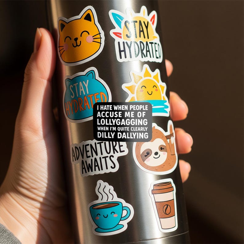 May include: A stainless steel water bottle covered in colorful stickers. The stickers feature a smiling cat, a sun, a sloth, a coffee cup, and the words "Stay Hydrated" and "Adventure Awaits." One sticker reads "I hate when people accuse me of lollygagging when I'm quite clearly dilly dallying."