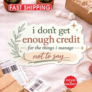 May include: A sticker or magnet with the text "i don't get enough credit for the things i manage not to say." The sticker has a decorative floral design. The image also shows small potted cacti and wrapped packages.