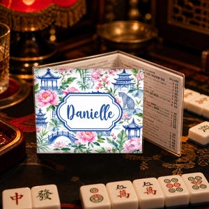 May include: A personalized Mahjong tile holder with a floral and pagoda design. The holder features a blue and white color scheme with the name "Danielle" in a white oval. Pink flowers and a leopard are also visible.