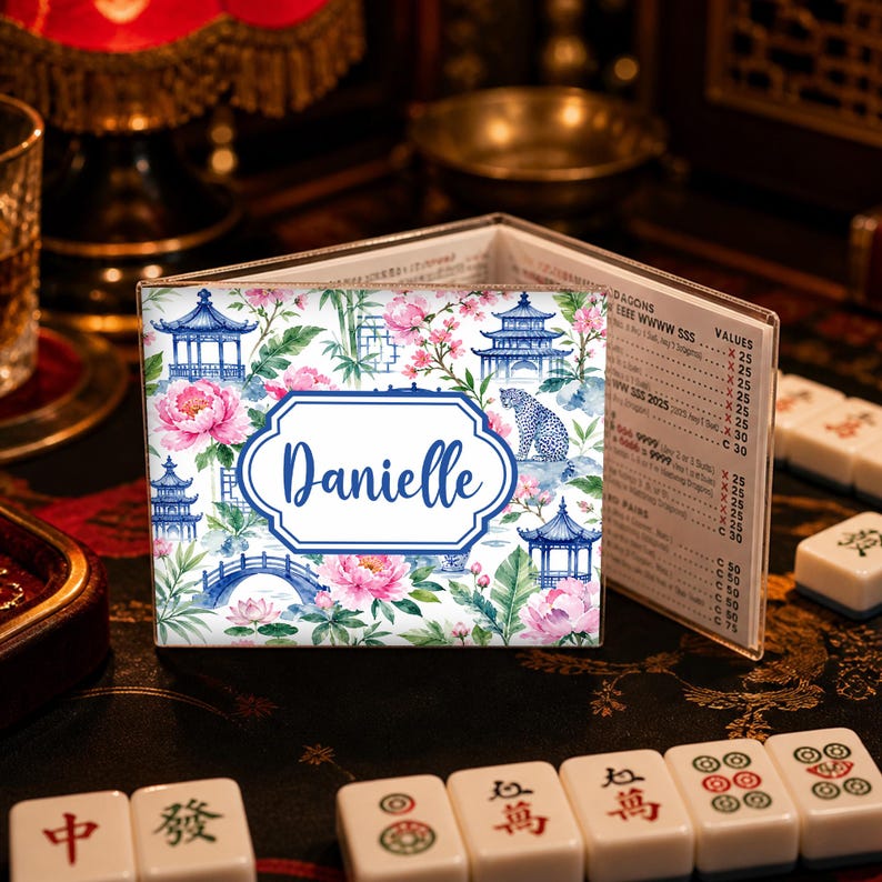 May include: A personalized Mahjong tile holder with a floral and pagoda design. The holder features a blue and white color scheme with the name "Danielle" in a white oval. Pink flowers and a leopard are also visible.