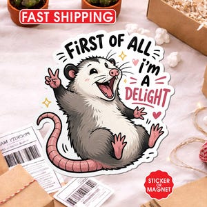 Puede incluir: Una pegatina o im&aacute;n con un dise&ntilde;o de zarig&uuml;eya de dibujos animados. La zarig&uuml;eya tiene una expresi&oacute;n alegre y un signo de la paz. El texto de la pegatina dice "First of all, I'm a Delight". La pegatina tiene un borde blanco.