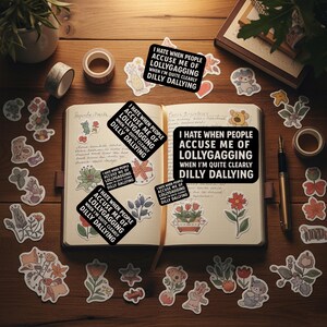 May include: An open notebook with stickers and stationery on a wooden surface. The stickers have a black background with white text that reads "I HATE WHEN PEOPLE ACCUSE ME OF LOLLYGAGGING WHEN I'M QUITE CLEARLY DILLY DALLYING". Decorative floral and animal stickers are scattered around.