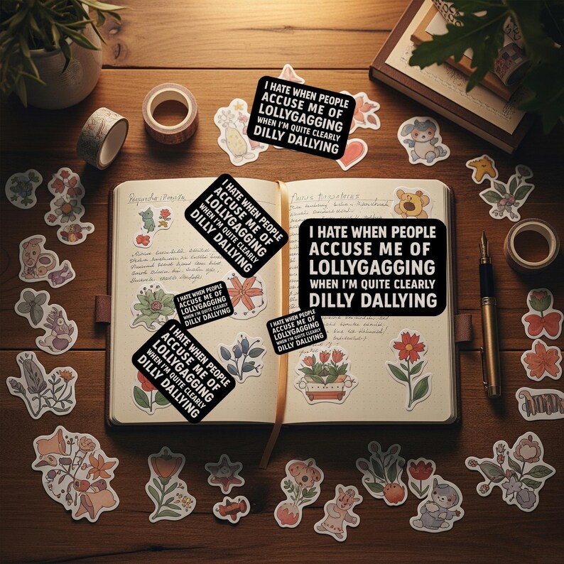 May include: An open notebook with stickers and stationery on a wooden surface. The stickers have a black background with white text that reads "I HATE WHEN PEOPLE ACCUSE ME OF LOLLYGAGGING WHEN I'M QUITE CLEARLY DILLY DALLYING". Decorative floral and animal stickers are scattered around.