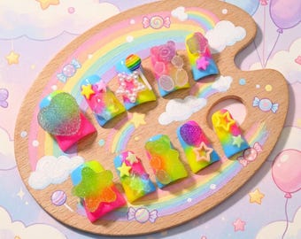 May include: A set of ten press-on nails featuring a vibrant rainbow gradient base. Each nail is decorated with three-dimensional embellishments including translucent gummy bear shapes, glittery hearts, colorful stars, and small white pearl accents.