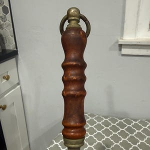 K&ouml;nnte beinhalten: Ein Messer mit einem Holzgriff und einer Metallklinge. Der Griff ist dunkelbraun mit Messingakzenten und einem Ring oben. Die Klinge ist silberfarben und hat eine sternf&ouml;rmige Basis.