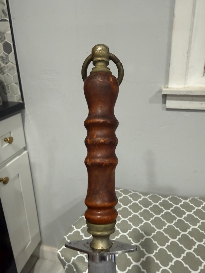 K&ouml;nnte beinhalten: Ein Messer mit einem Holzgriff und einer Metallklinge. Der Griff ist dunkelbraun mit Messingakzenten und einem Ring oben. Die Klinge ist silberfarben und hat eine sternf&ouml;rmige Basis.